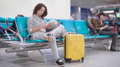 年轻的黑发女子在机场的智能手机上使用免费无线上网，而她的手提箱就在机场附近